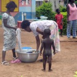 Women washing clothes outdoors while child watches
