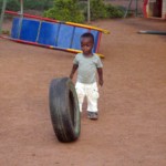 Child rolling a tire on dirt playground